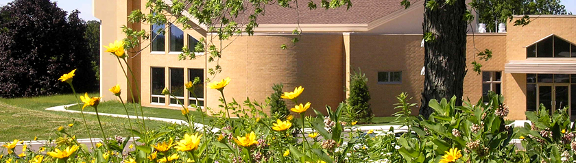 Front door and windows of Holy Wisdom Monastery seen through yellow spring flowers blooming in the surrounding prairie